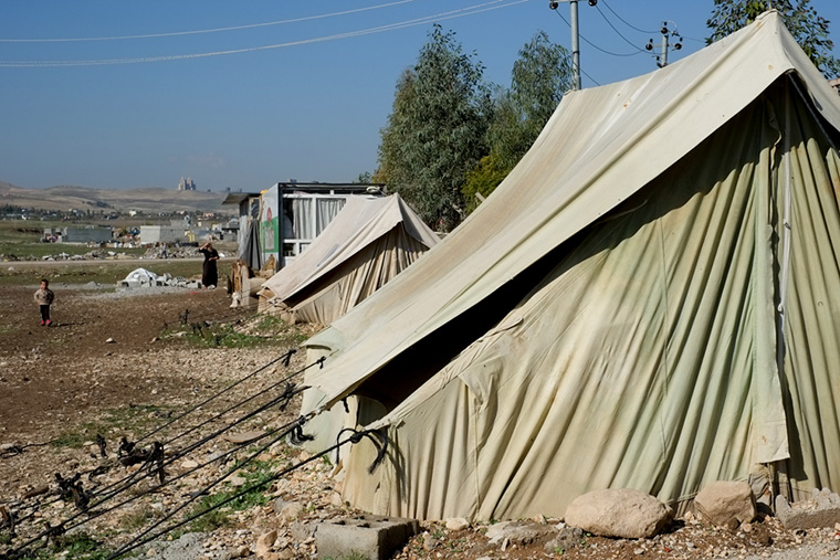 Tents and shipping containers, now home to displaced Iraqi families, line a boundary fence.