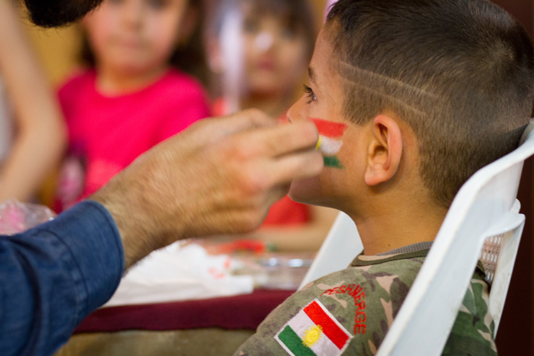 A young boy dressed in military fatigues gets the Kurdish flag painted on his face during an Easter party hosted by a local Assyrian church.