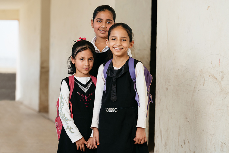 Three Iraqi girls wear school uniforms and backpacks...they are excited to go to school!