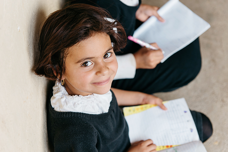 A young girl looks up from her school book and smiles.