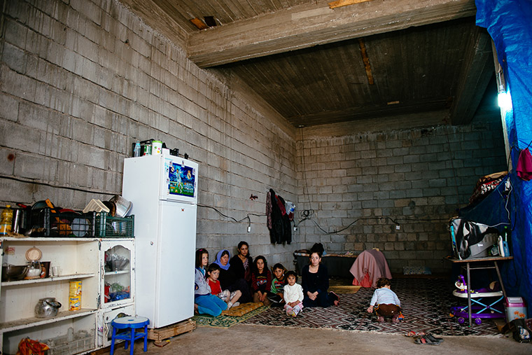A Yazidi family, IDPs in Iraq, sit inside their temporary home—an unfinished concrete warehouse