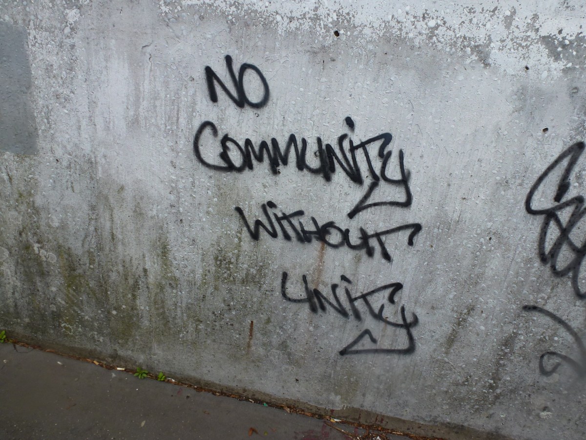 Black graffiti on a gray wall reads "No community without unity"